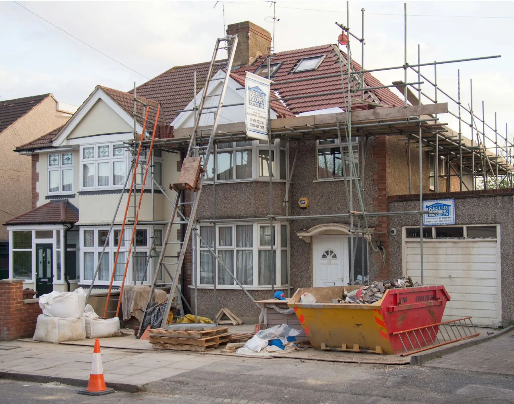 A house under construction with scaffolding and a skip outside