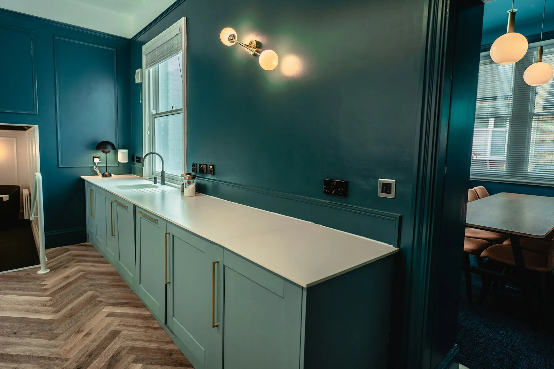 A dark green fitted kitchen with herringbone wood flooring