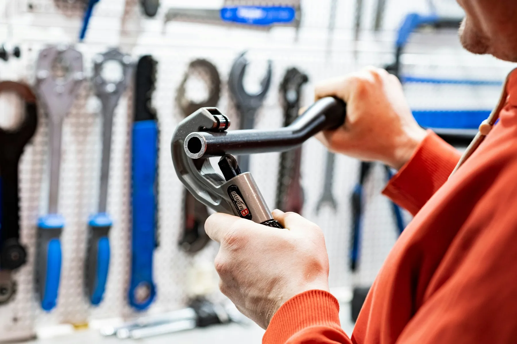 A plumber using a pipe wrench, with tools racked on the wall behind